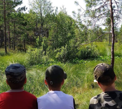 Lapset istuu kesäisen metsän reunalla.