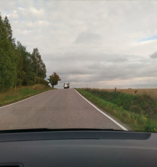 Auton ikkunasta otettu kuva, jossa edellä ajaa liikkuvan nuorisotyön matkailuauto, ympärillä peltomaisema. Kuvaaja: Aino Tormulainen.